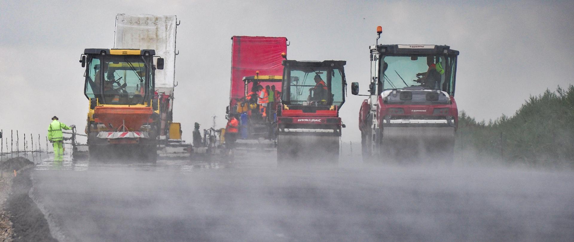 Budowa drogi ekspresowej. Widać walce oraz osoby pracujące przy układaniu nawierzchni drogi.