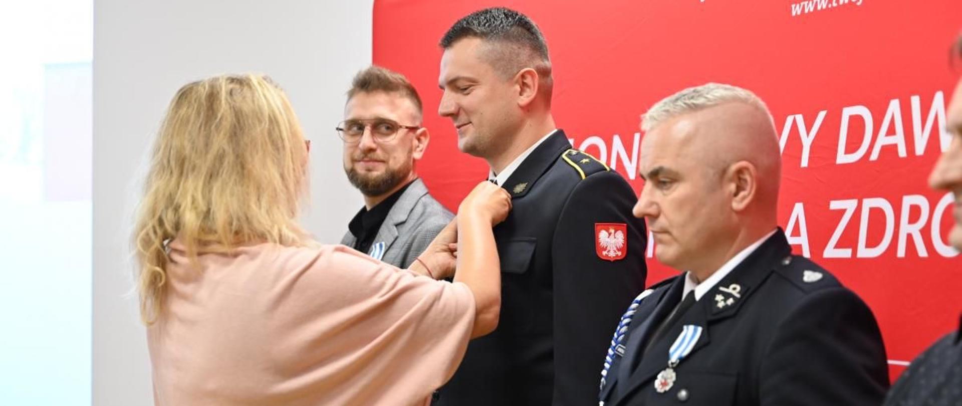 Odznaczony strażak w mundurze w trakcie przypinania medalu do munduru przez Dyrektor RCK w Gdańsku