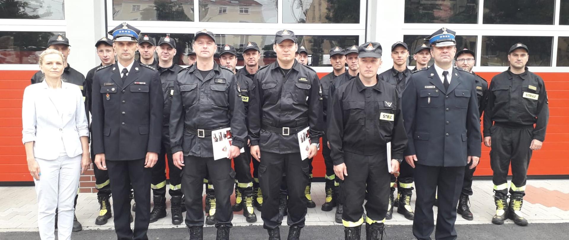 Awanse w kościańskiej Komendzie. Na zdjęciu stoją strażacy i pracownicy komendy, w tle budynek Komendy.