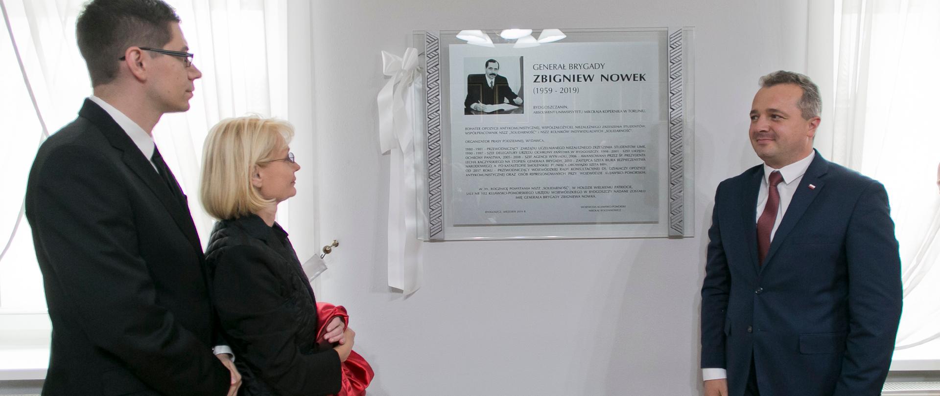 trzy osoby przy tablicy pamiątkowej 