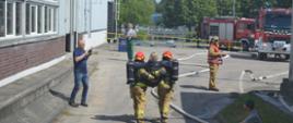 Zdjęcie przedstawia ewakuację przez strażaków jednej z osób poszkodowanych oraz rozjemcę ćwiczeń na tle samochodów pożarniczych