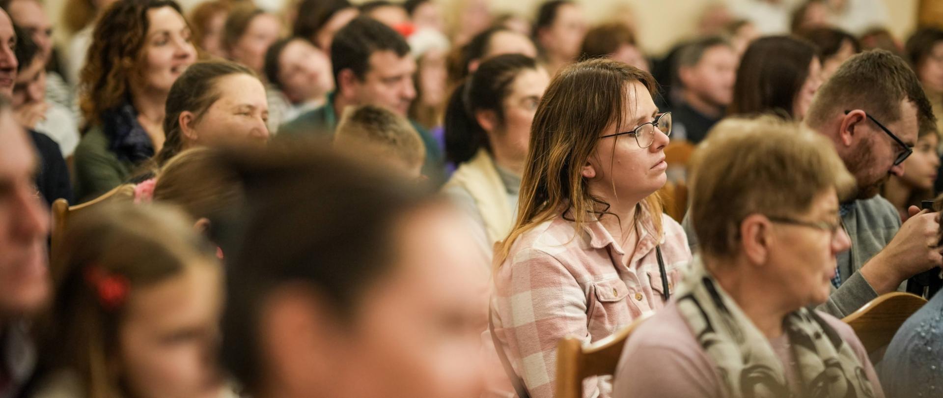 publiczność w sali koncertowej szkoły siedząca na krzesłach i słuchająca koncertu bądź innego wystąpienia