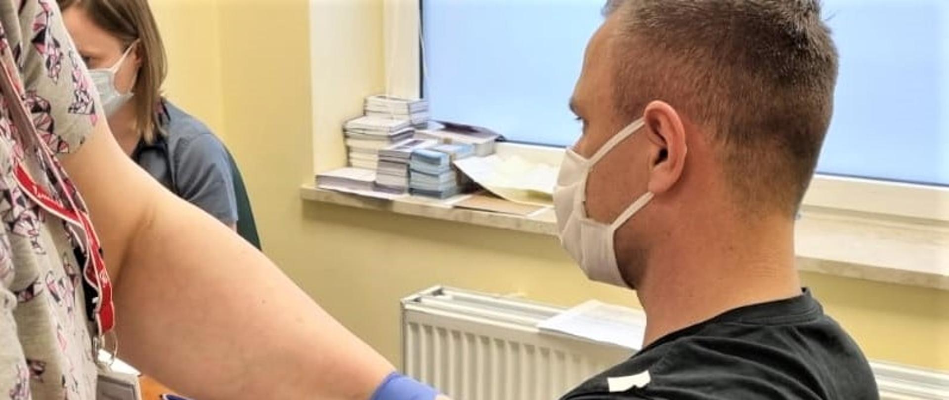 Zdjęcie przedstawia funkcjonariusza PSP podczas szczepienia. 