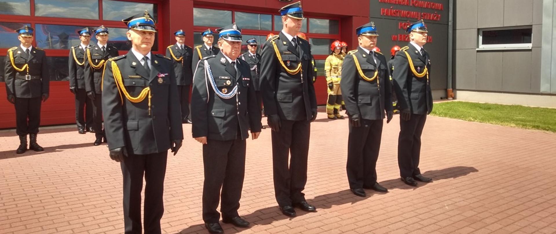 na zdjęciu plac przed budynkiem Komendy Powiatowej PSP w Brzezinach podczas uroczystej zbiórki z okazji Dania Strażaka, na środku stoi czterech funkcjonariuszy komendy oraz prezes zarządu oddziału powiatowego ZOSP RP w Brzezinach odznaczonych złotą i brązowymi odznakami "Zasłużony dla ochrony przeciwpożarowej"