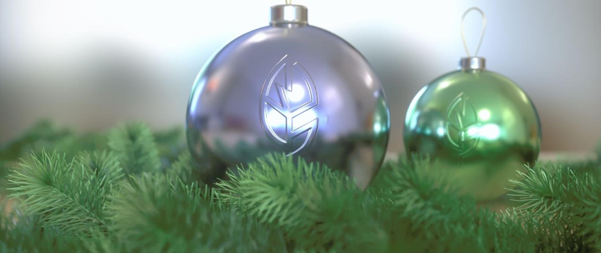 Gałązki świerku a na nich 2 bombki z logo Regionalnej Dyrekcji Ochrony Środowiska w Olsztynie. Jedna większa koloru fioletowego, druga mniejsza koloru zielonego.