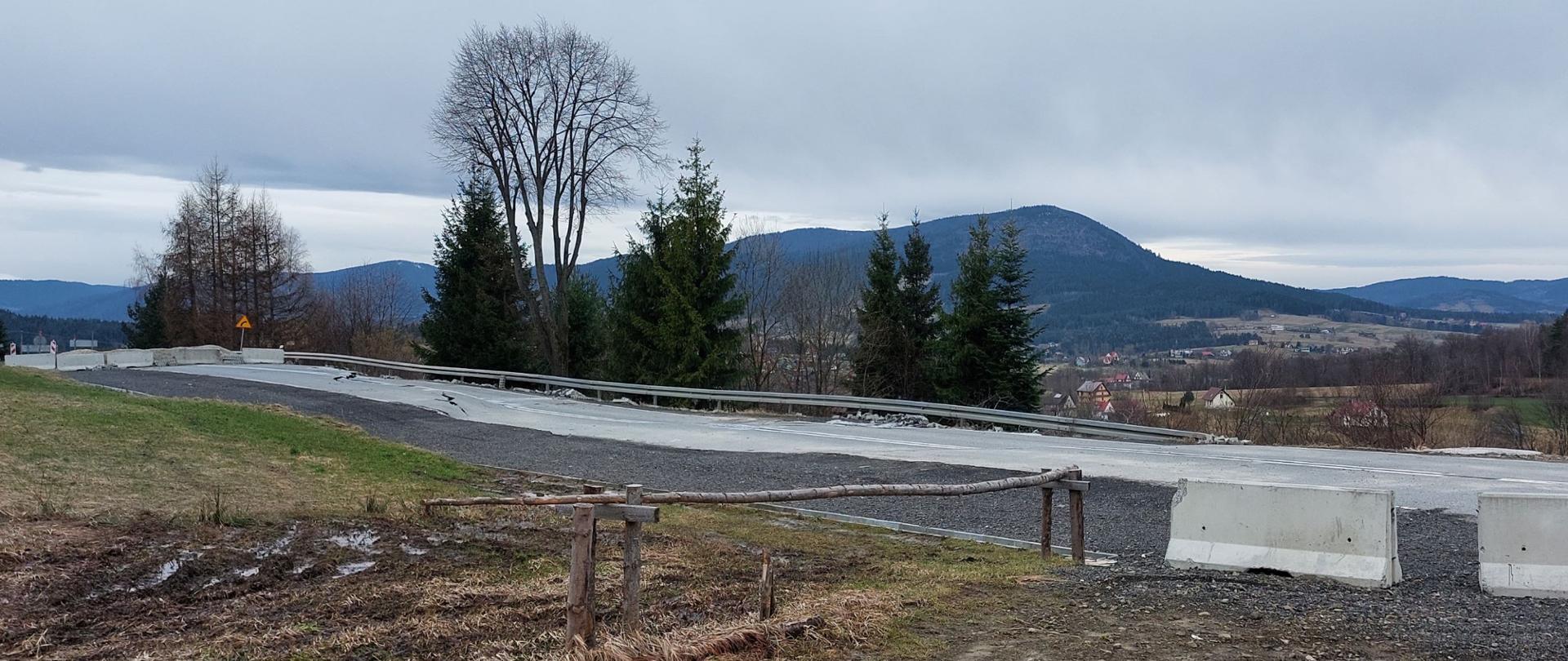 zdjęcie osuwiska na DK28 w Kasinie Wielkiej zrobione 22 lutego 2024 roku, na jezdni znaczne pęknięcia, droga jest przekrzywiona i pochylona. w tle Beskidy