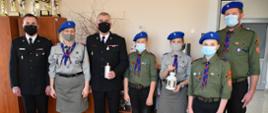 Zdjęcie obrazuje harcerzy ZHP Hufca Skarżysko-Kamienna, którzy przekazali Komendantowi Powiatowemu PSP w Skarżysku-Kamiennej Betlejemskie Światło Pokoju. Ze względu na trwającą pandemię wszyscy uczestnicy spotkania mają zasłonięte usta i nos maseczkami ochronnymi.