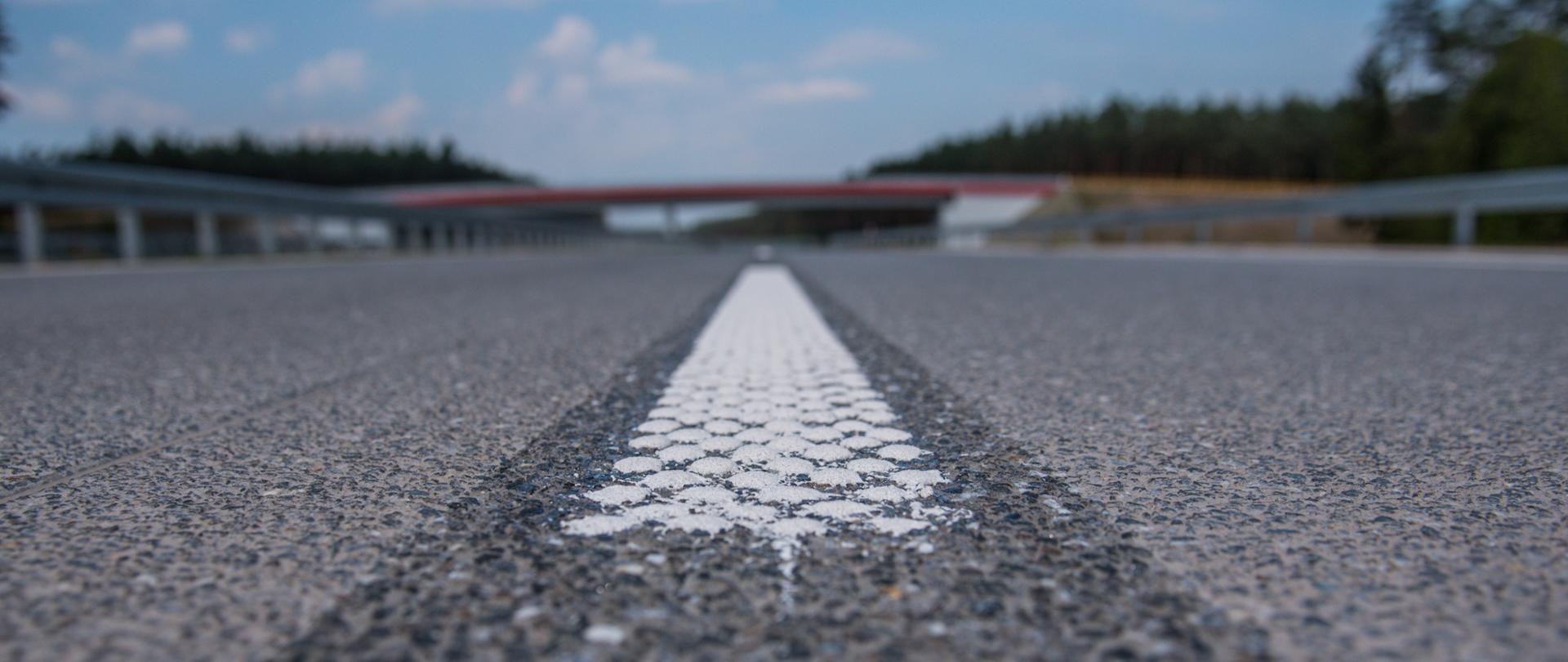 Fotografia nawierzchni mineralno-asfaltowej drogi z poziomu gruntu. 