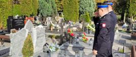 dwóch strażaków stoi pomiędzy grobami oddając hołd zmarłemu funkcjonariuszowi