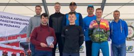 Na zdjęciu widać kilku mężczyzn w ubraniu sportowym i cywilnym znajdujących się na scenie oraz podeście podczas wręczania nagród w zawodach biegowych. Panowie to funkcjonariusze Państwowej Straży Pożarnej. 