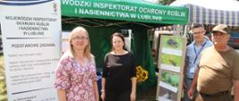 Dwie kobiety i dwóch mężczyzn stoi przed namiotem. Obok nich stojak reklamowy oraz wystawa przedstawiająca szkodniki