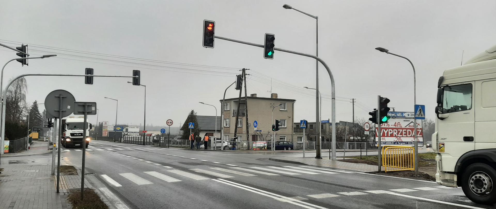 Skrzyżowanie drogi krajowej nr 11 z drogami gminnymi w miejscowości Zielona Łąka. Widoczne samochody i zabudowania jednorodzinne.