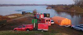 Samochody oraz sprzęt Państwowej Straży Pożarnej ustawione są na brzegu rzeki Wisła.