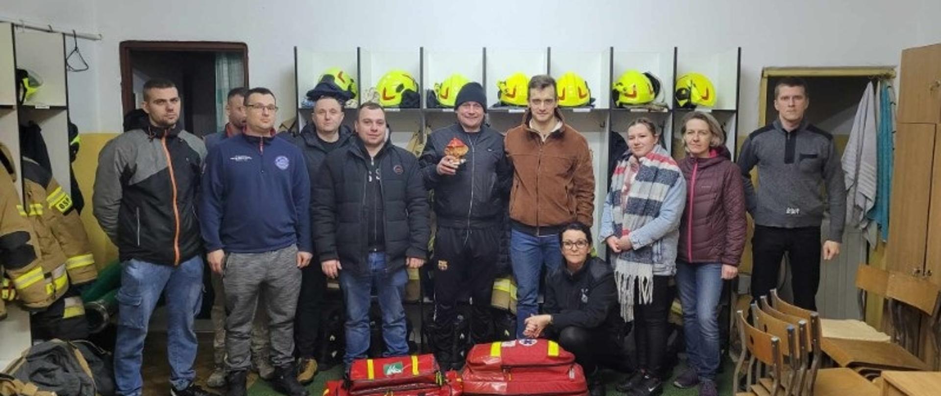 Strażacy stoją w rzędzie, przed nimi dwie torby z wyposażeniem do pierwszej pomocy.