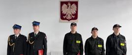 Trzech nowo przyjętych strażaków oraz dwóch strażaków kończących trzyletni okres służby przygotowawczej. Strażacy stojący w szeregu.