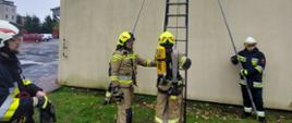 druhowie w trakcie ćwiczenia z drabin przystawnych, strażak przygotowuje się do wejścia na drabinę opartą o elewację budynku