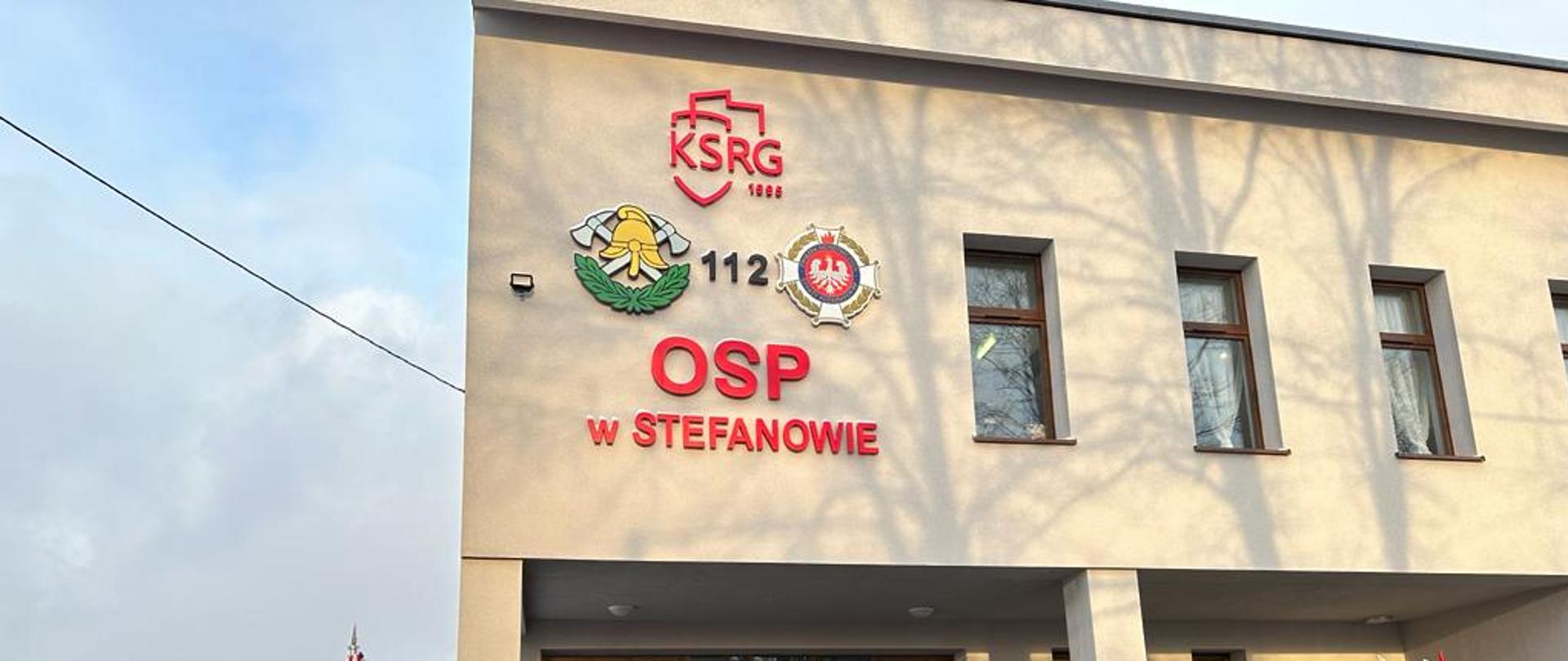 zdjęcie przedstawia gości, druhów OSP i funkcjonariuszy PSP na tle strażnicy OSP w Stefanowie. Od lewej stoją: Wójt Gminy Brójce Radosław Agaciak, Wiceminister Sprawiedliwości Piotr Cieplucha, Prezes OSP Stefanów Marek Muras, Naczelnik OSP Stefanów Karol Olban, z-ca Komendanta Wojewódzkiego PSP w Łodzi st.bryg. Paweł Malinowski, z-ca Komendanta Powiatowego PSP st.bryg. Tomasz Zabrzewski. Z lewej strony zdjęcia poczet flagowy z OSP stefanów i pooddział druhów z jednostki, wszyscy w mundurach OSP. 