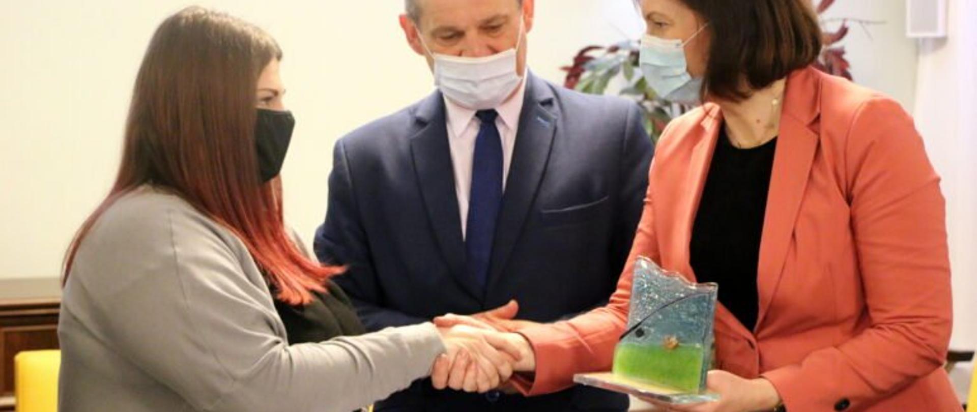 Wojewoda podkarpacki Ewa Leniart gratuluje uczestniczce ochotniczych hufców pracy. W środku stoi komendant wojewódzki Ochotniczych Hufców Pracy Jerzy Cypryś. 