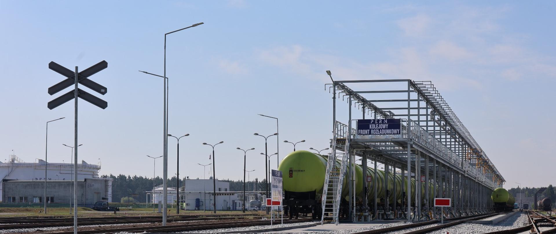Na zdjęciu widać w całości kolejowy front rozładunkowy w Nowej Wsi Wielkiej. Obok frontu stoi pociąg towarowy w formie cysterny. Widzimy znak informujący o przecinających się torach.