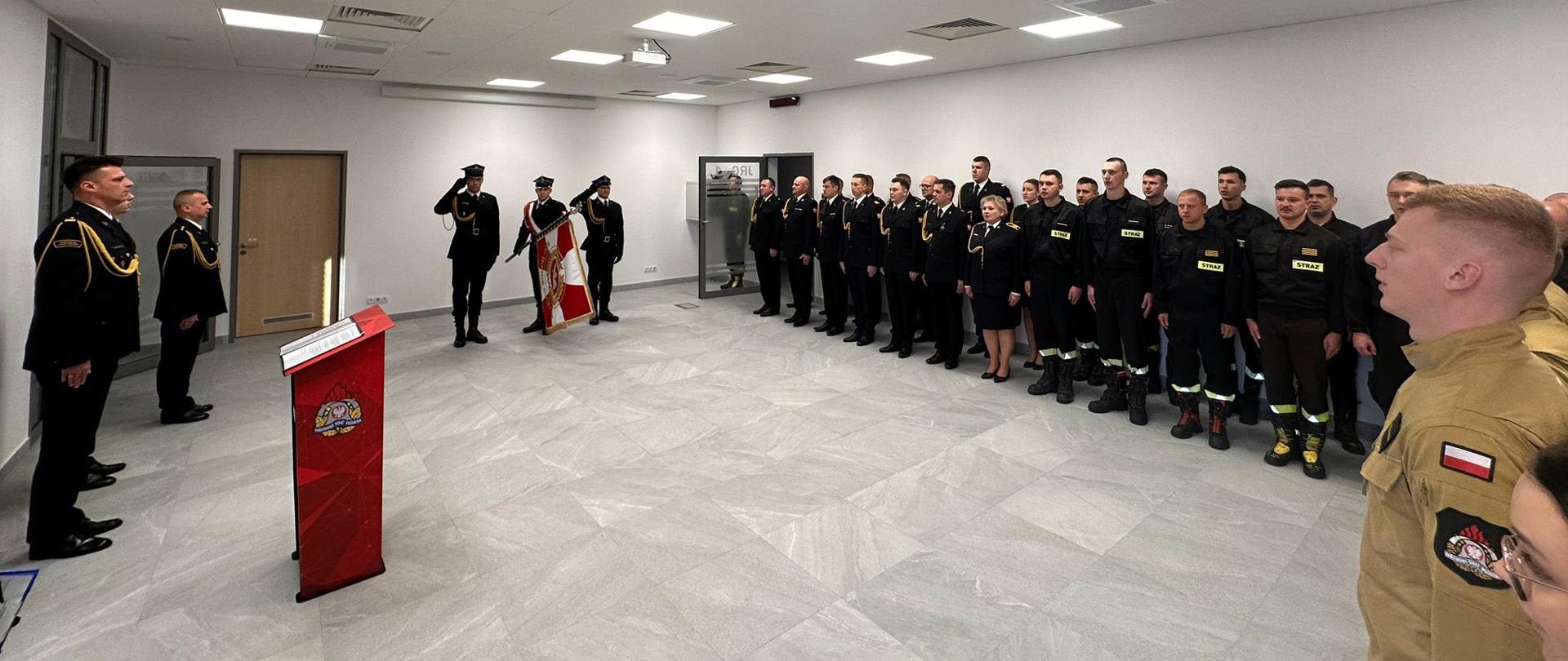 W sali tradycji funkcjonariusze stoją ubrani w mundury wyjściowe, w centralnej części poczet sztandarowy prezentuje sztandar komendy.