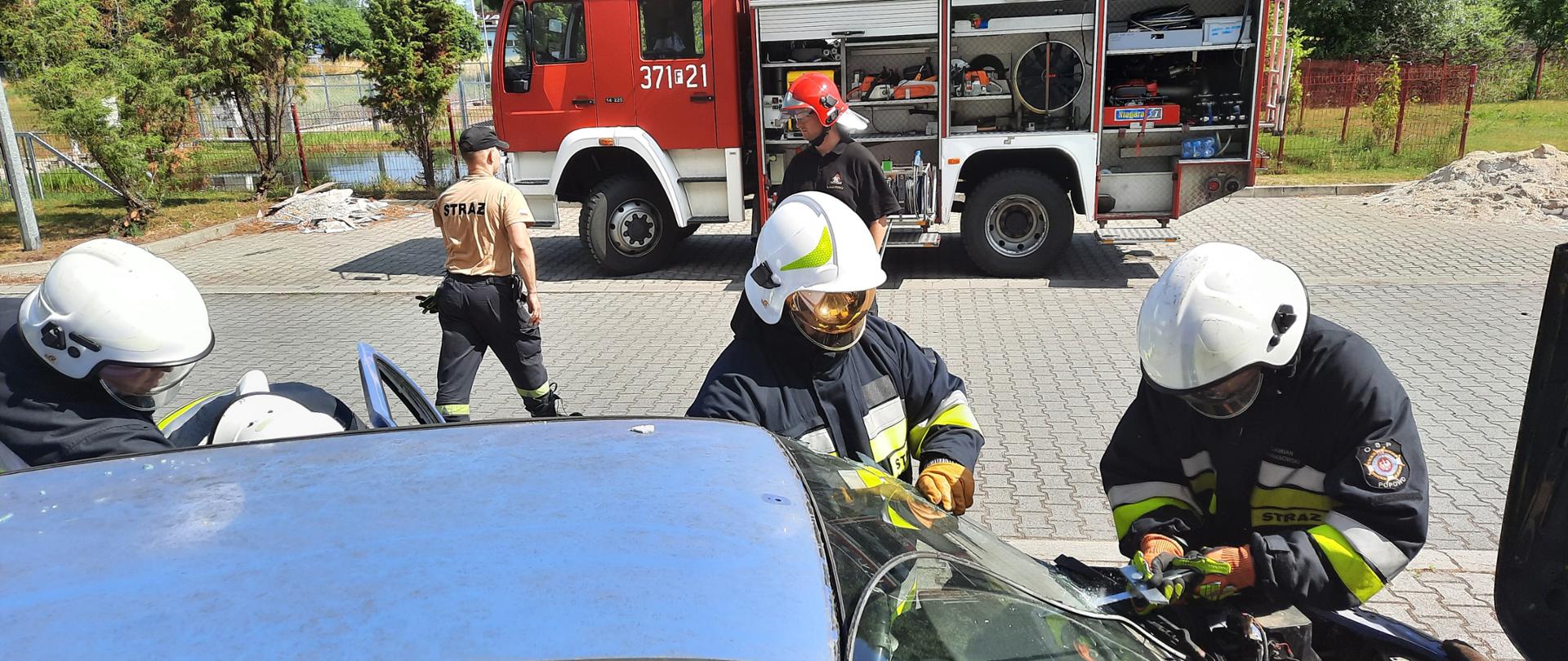 Zdjęcie przedstawia ratowników podczas usuwania szyby przedniej w pojeździe.