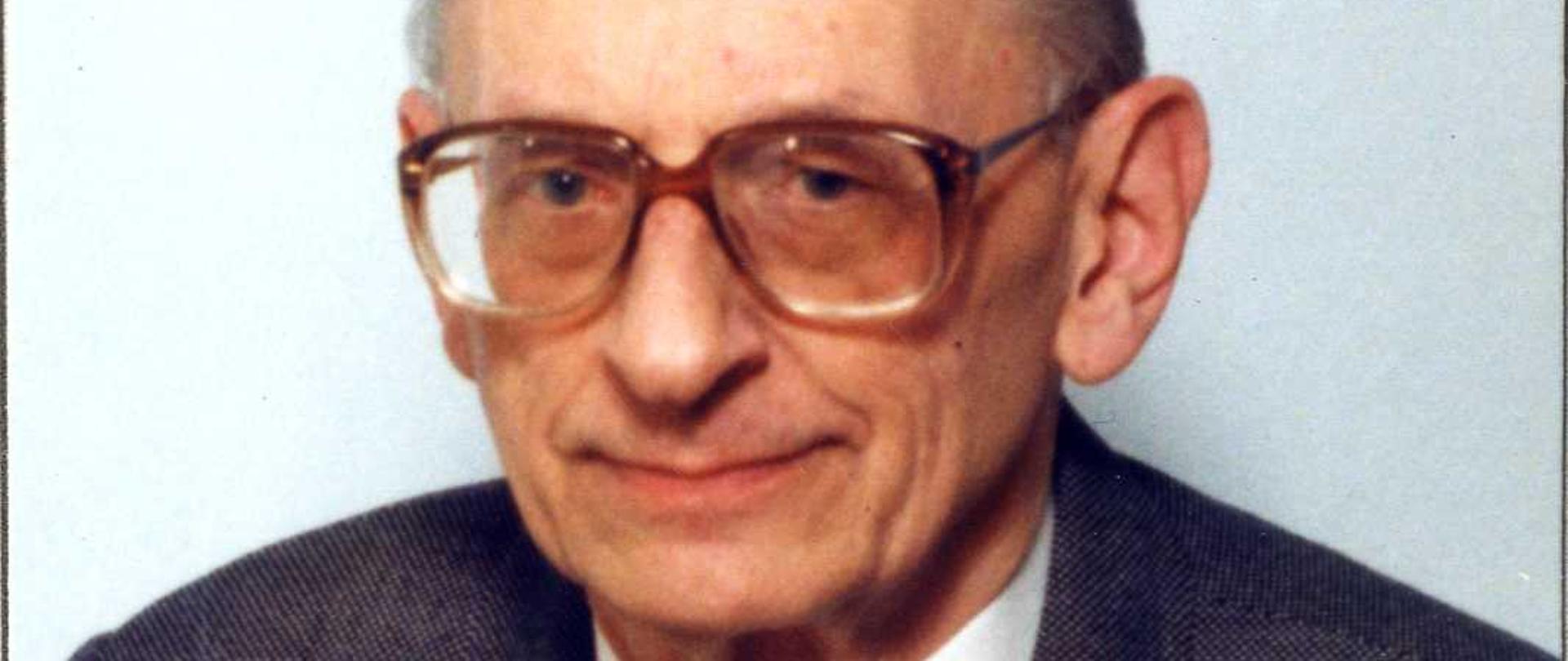 Władysław Bartoszewski kolorowy portret łysiejącego mężczyzny w okularach z grubymi oprawkami, siwe włosy, ciemna marynarka, ciemny krawat w drobne ciemne wzory.