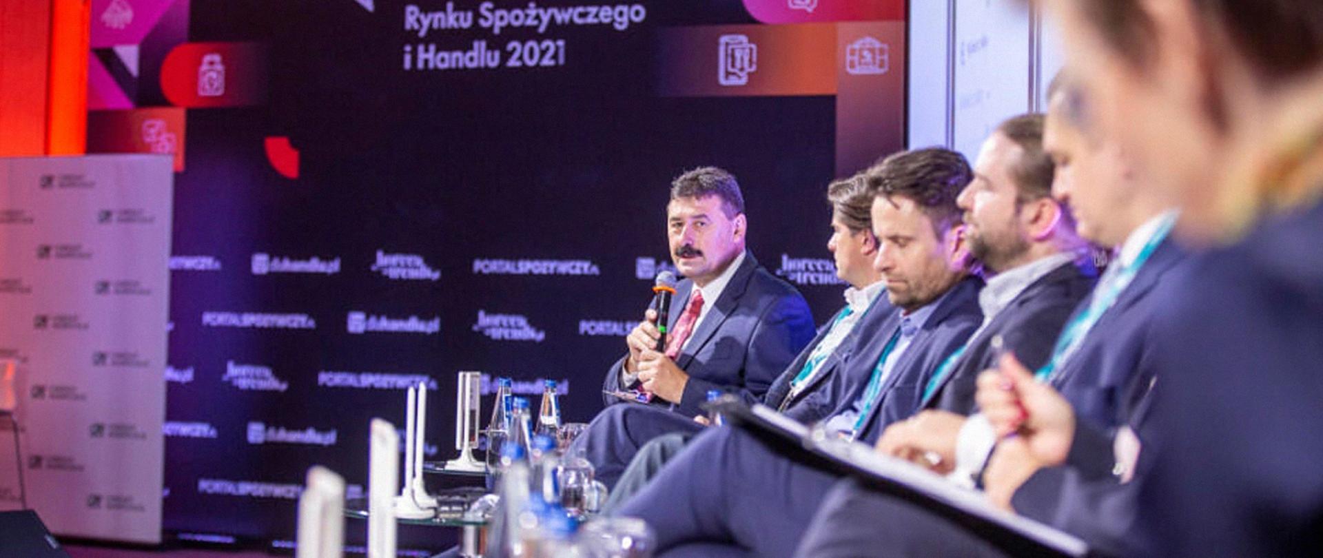 Sekretarz stanu Ryszard Bartosik z mikrofonem w dłoniach, siedzący wśród uczestników Forum Rynku Spożywczego i Handlu 2021.