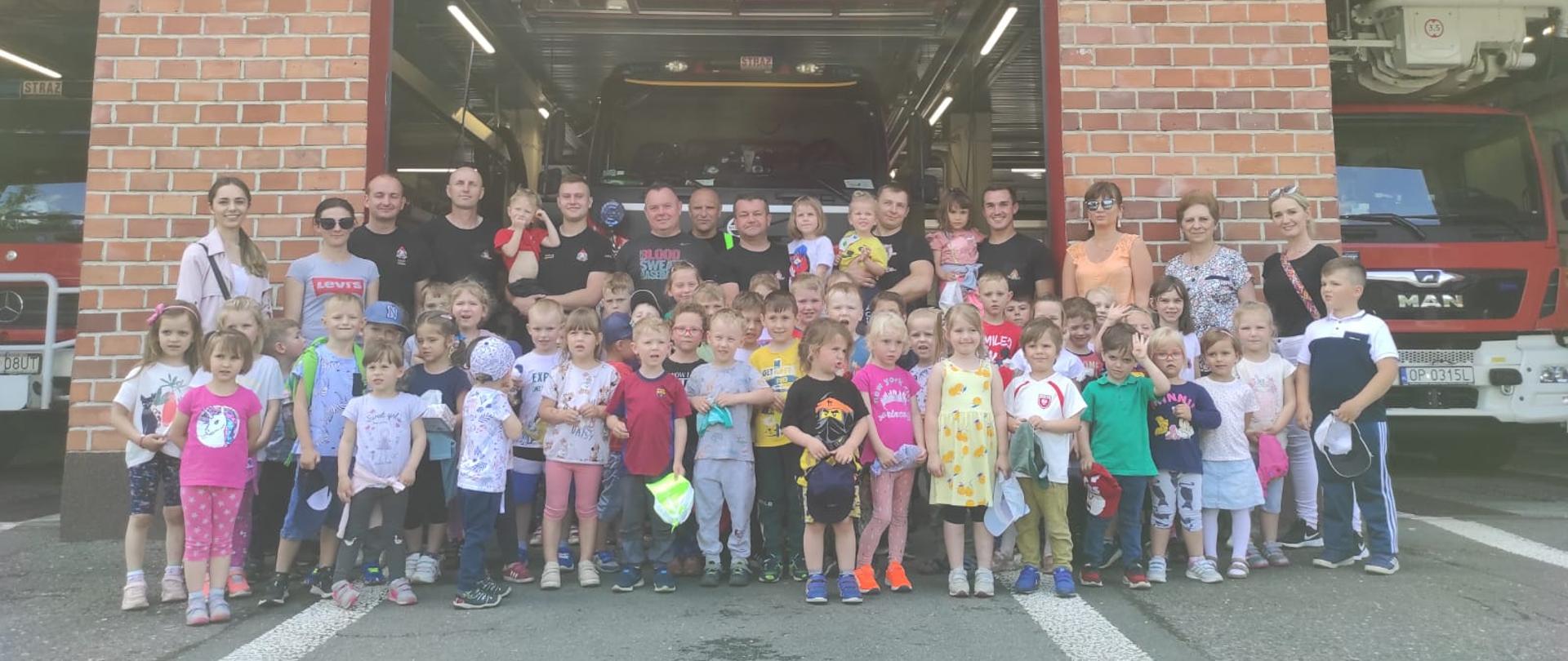 Na zdjęciu znajdują się dzieci ustawione do zdjęcia zbiorowego wraz z opiekunami na tle ga