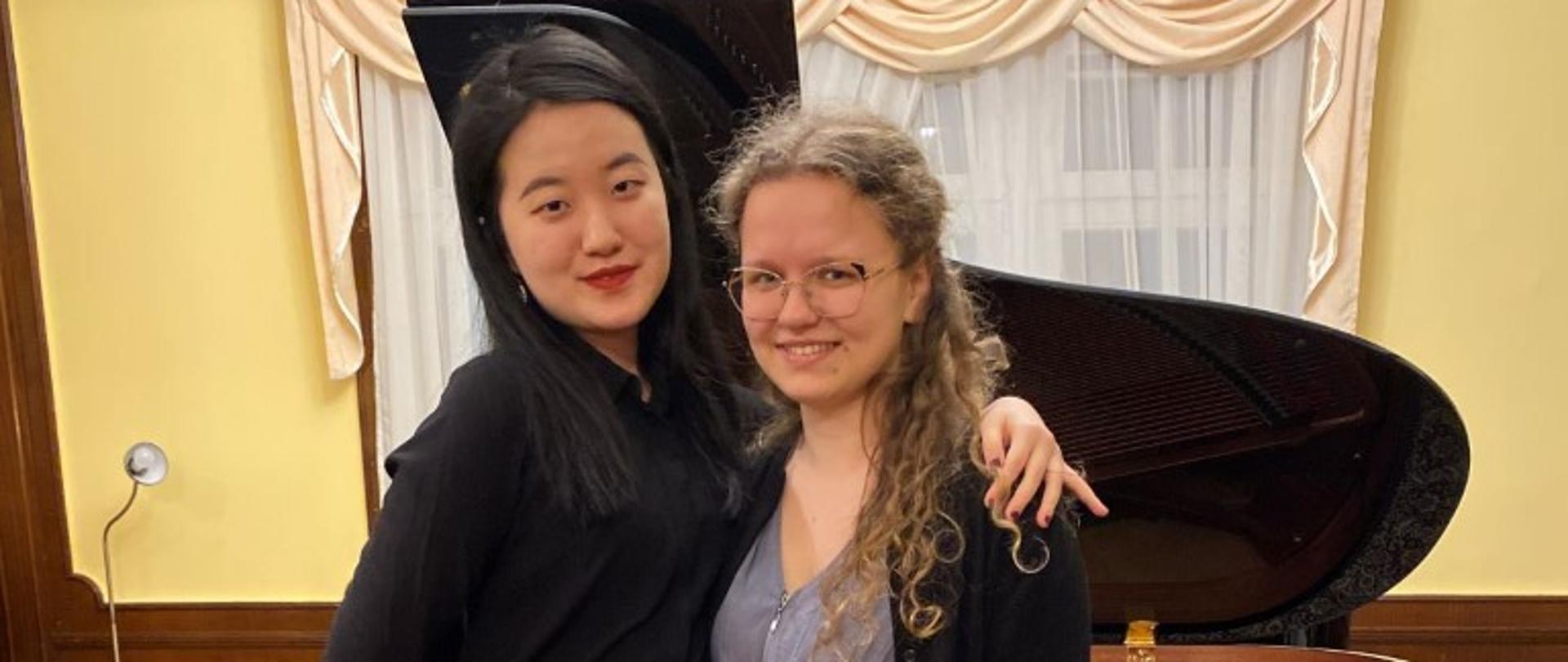 Zdjęcie kolorowe. Dwie uczestniczki koncertu stoją na tle fortepianu w sali kameralnej Państwowej Szkoły Muzycznej I i II stopnia w Słupsku.