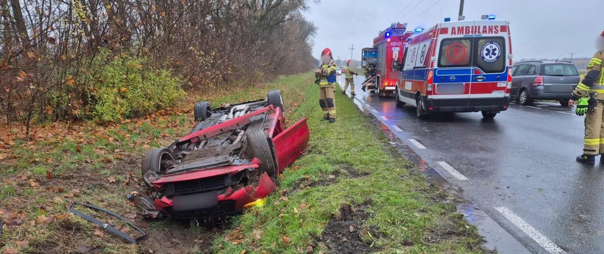 Na zdjęciu znajduje się wrak pojazdu oraz karetka pogotowia i strażacy w nomexach.