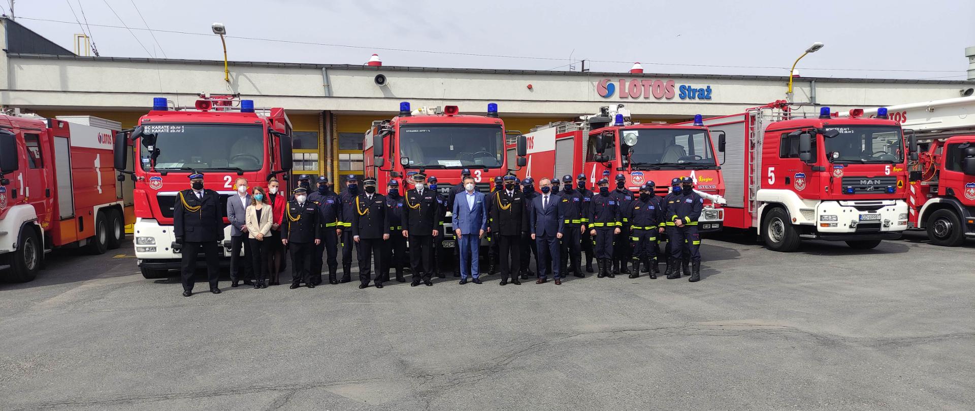 Pracownicy Lotos Straż Sp. z o.o. oraz kierownictwo KW PSP w Gdańsku stoją na tle samochodów ratowniczo-gaśniczych.