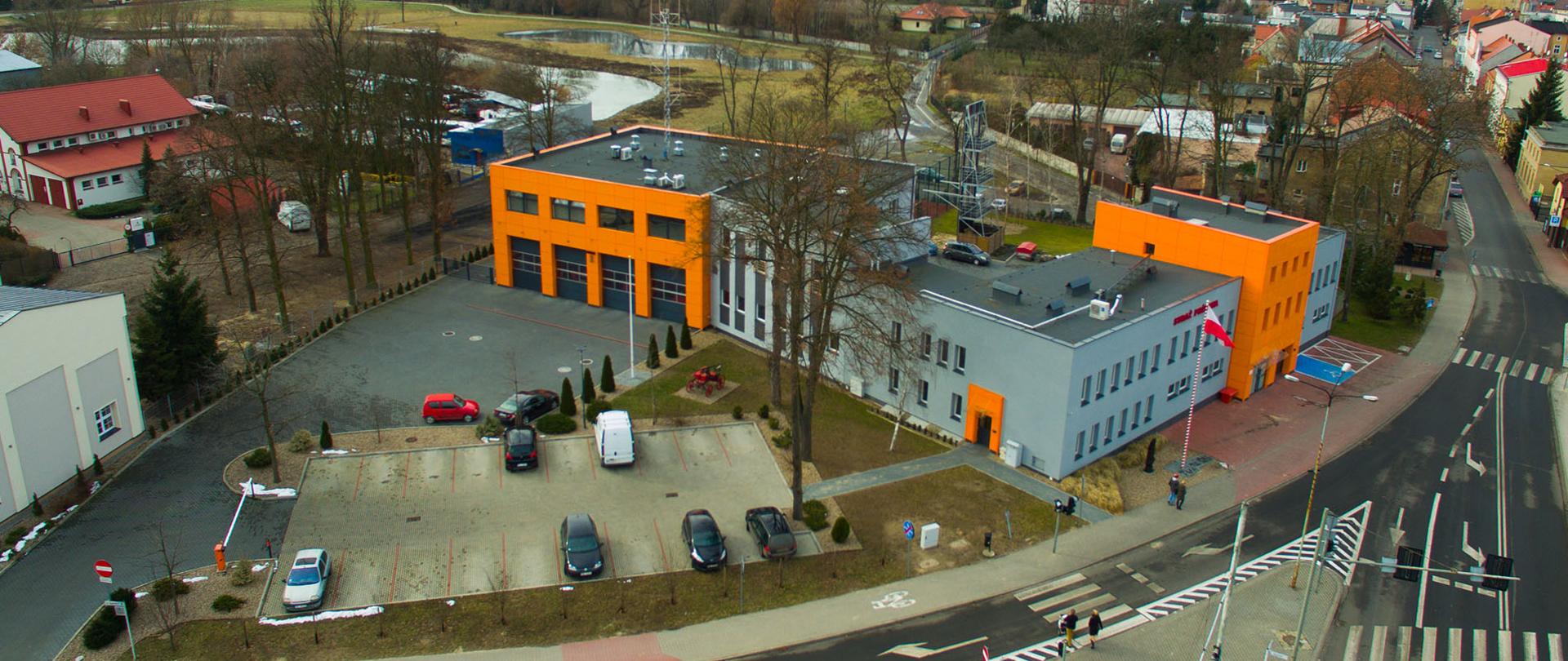 Widok z góry na budynek wolsztyńskiej komendy. W tle, panorama miasta Wolsztyn. Na parkingu przed budynkiem zaparkowane samochody. Ulice puste. Krajobraz jesienny.