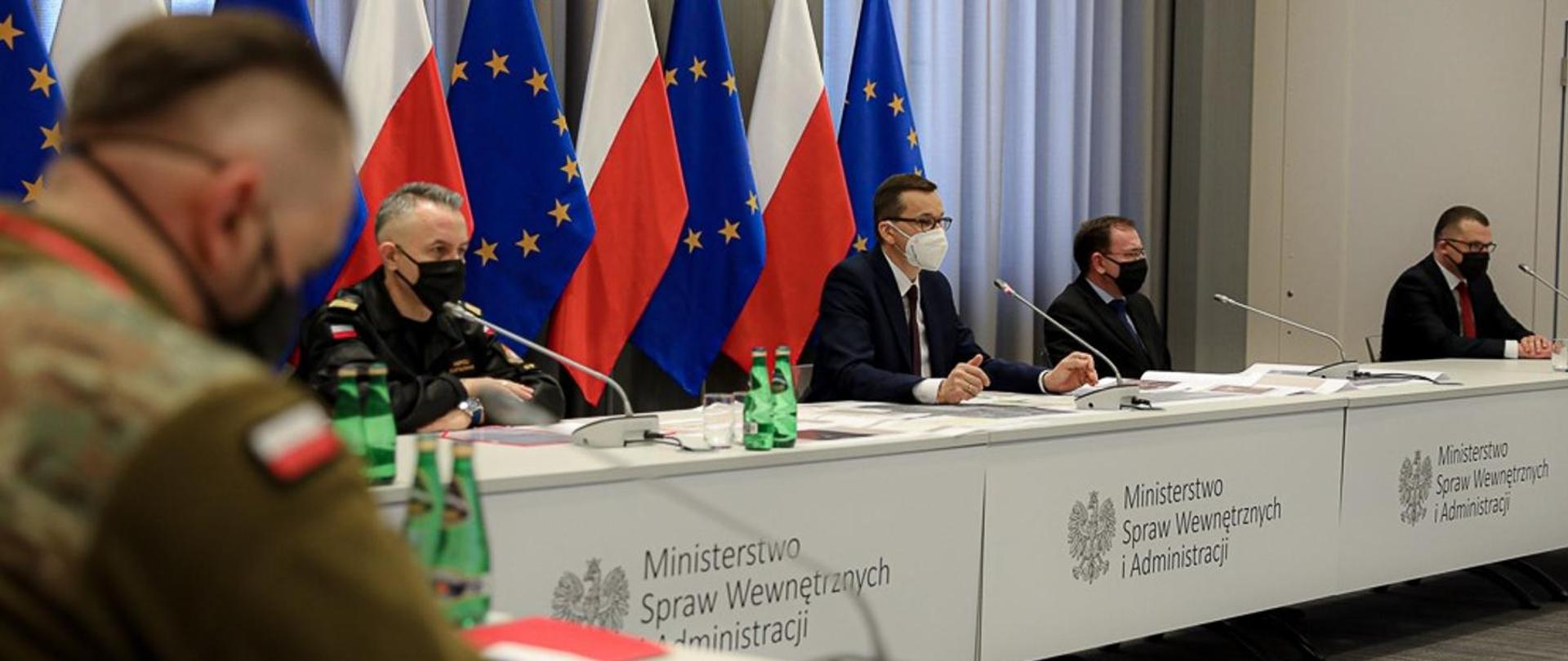 Na zdjęciu 4 mężczyzn siedzących za stołem. Od lewej komendant główny Państwowej Straży Pożarnej nadbrygadier Andrzej Bartkowiak, premier Mateusz Morawiecki, minister spraw wewnętrznych i administracji Mariusz Kamiński, minister infrastruktury Andrzej Adamczyk