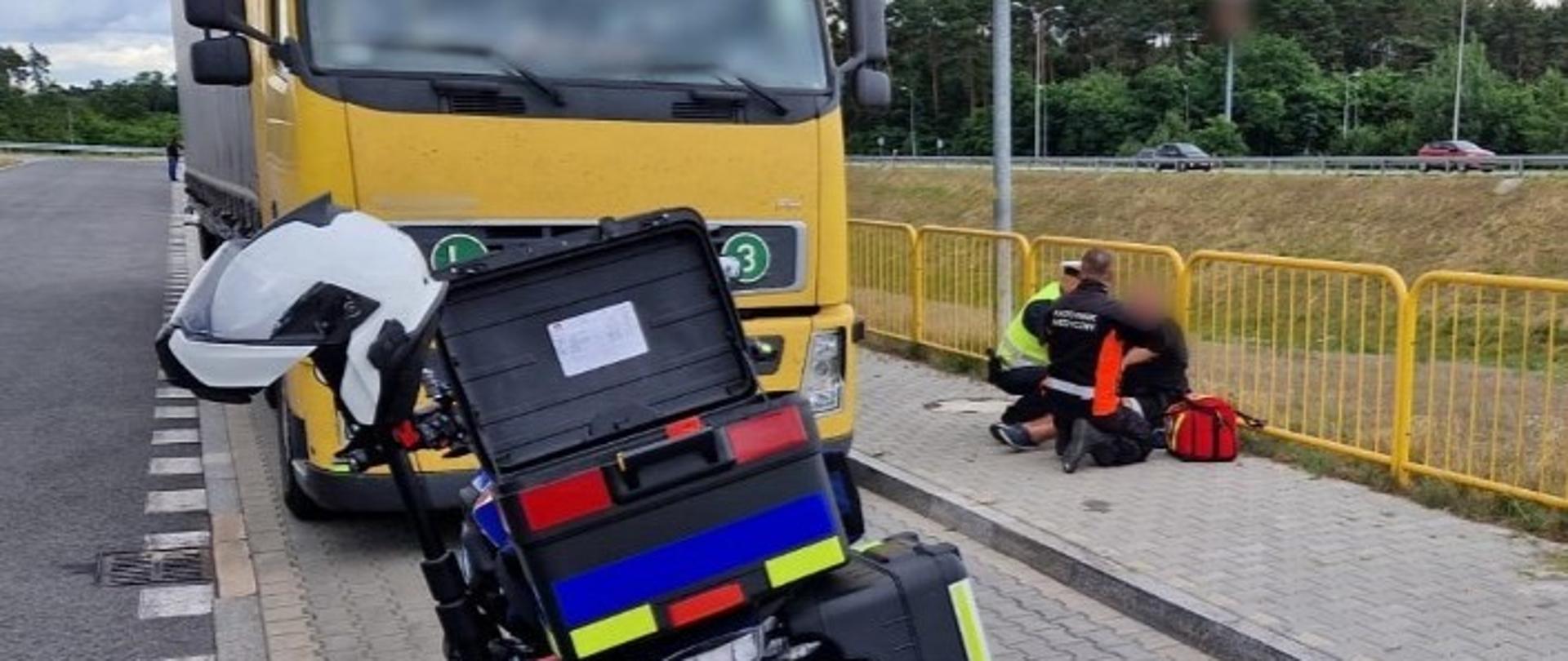 Inspektor lubuskiej ITD i ratownik medyczny udzielają pomocy kierowcy ciężarówki, który siedzi na chodniku. Obok, w zatoce parkingowej, stoi ciągnik siodłowy z naczepą. Przed ciężarówką stoi motocykl ratownictwa medycznego.