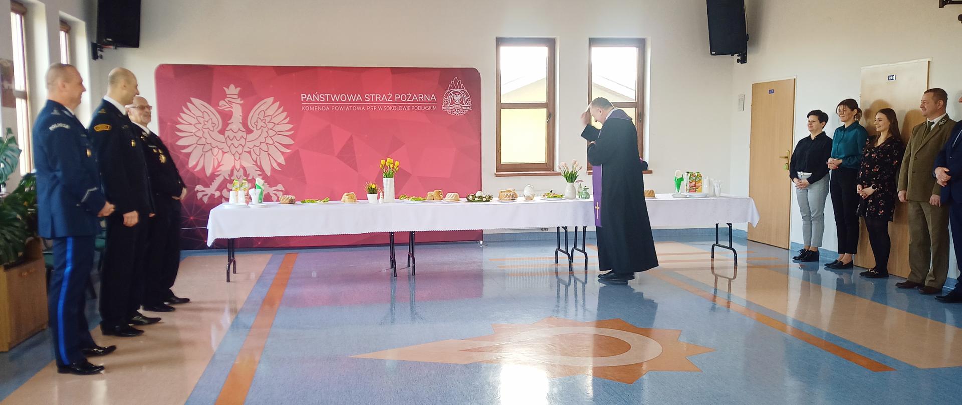 Spotkanie Wielkanocne w Komendzie Powiatowej PSP w Sokołowie Podlaskim 2024 - w sali komendy trwa święcenie pokarmu przez księdza