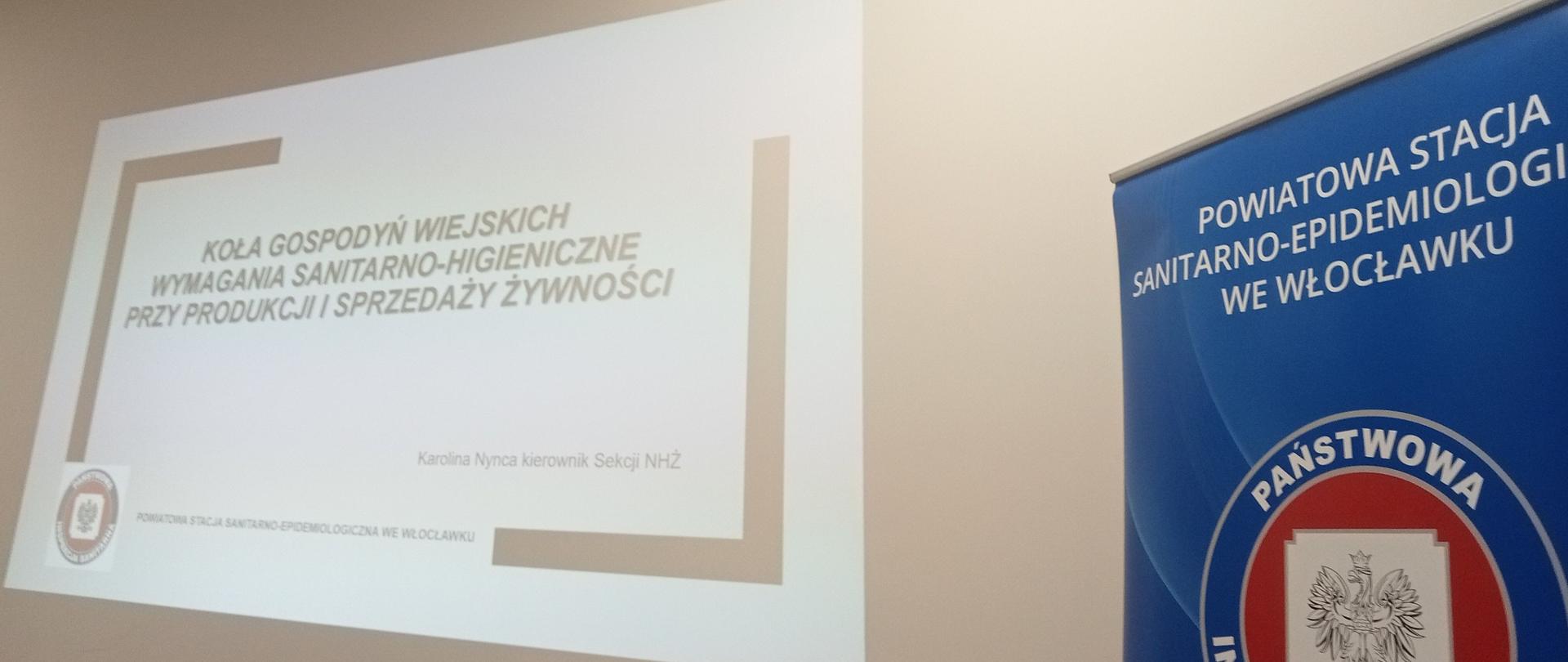 Na zdjęciu z prawej strony znajduje się baner Powiatowej Stacji Sanitarno-Epidemiologicznej we Włocławku.
Po lewej stronie tablica ukazująca tytuł prelekcji „KOŁA GOSPODYŃ WIEJSKICH WYMAGANIA SANITARNO-HIGIENICZNE PRZY PRODUKCJI I SPRZEDAŻY ŻYWNOŚCI”
