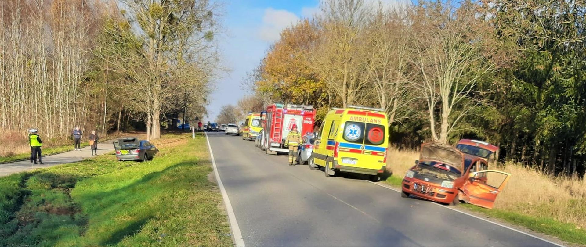 Zdjęcie przedstawia wypadek dwóch aut, oraz służby ratownicze pomagające w usunięciu zdarzenia. 