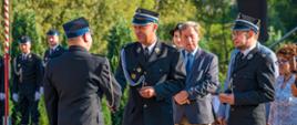 Widok z boku. Wójt gminy Brzeżnica wręcza strażakowi OSP kluczyki do samochodu. Po prawej stronie Poseł na Sejm RP przygotowany do wręczenia dowodu rejestracyjnego, a obok niego Przewodnicząca Rady Powiatu Wadowickiego. Za Wójtem przygotowany do przekazania gratulacji Senator RP. Z lewej strony zdjęcia w tle dwóch członków pocztu flagowego. 