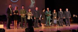 Na pierwszym planie widać dziesięć osób, cześć z nich trzyma statuetki. 
