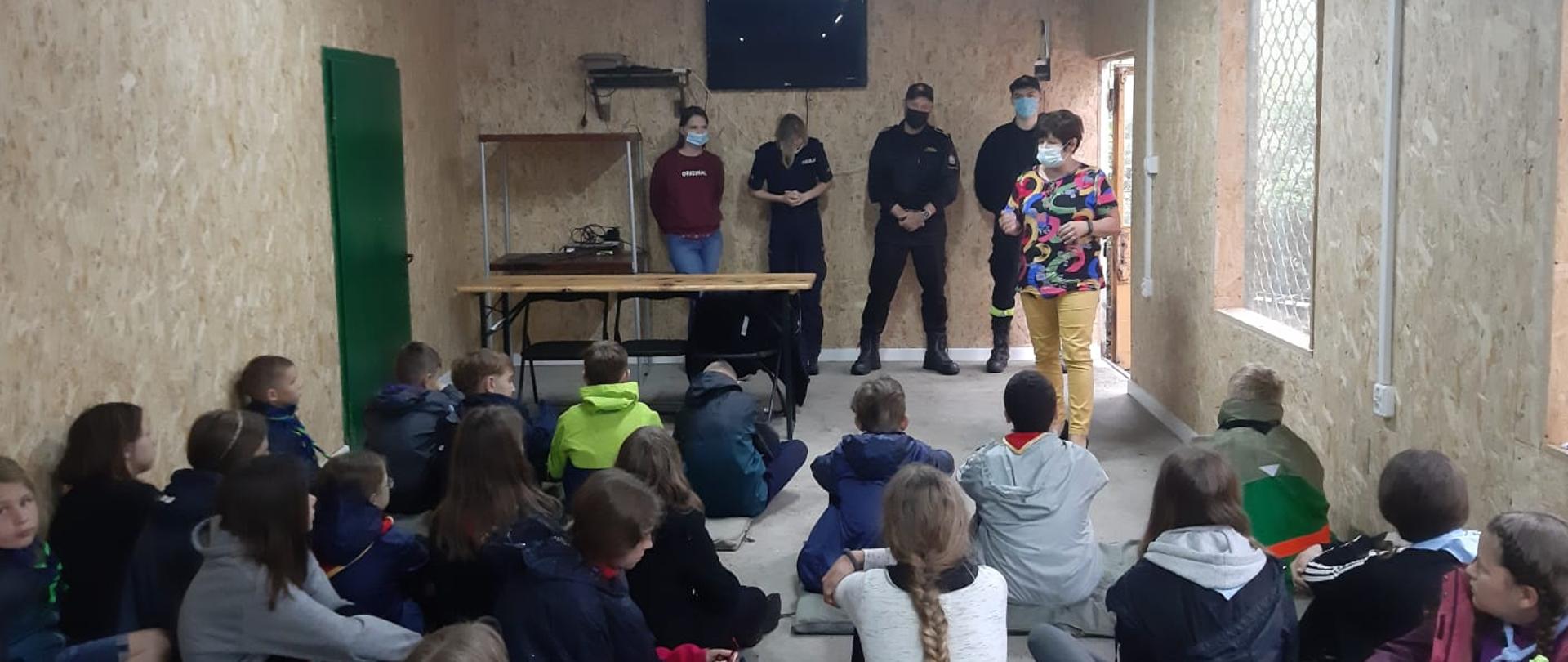 Zdjęcie przedstawia sale w której siedzi na podłodze młodzież i słucha wykładu prowadzonego przez strażaków.