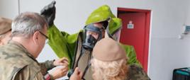 Na zdjęciu widoczni są żołnierze WOT w trakcie ubierania jednego w żołnierzy w chemiczne ubranie gazoszczelne.