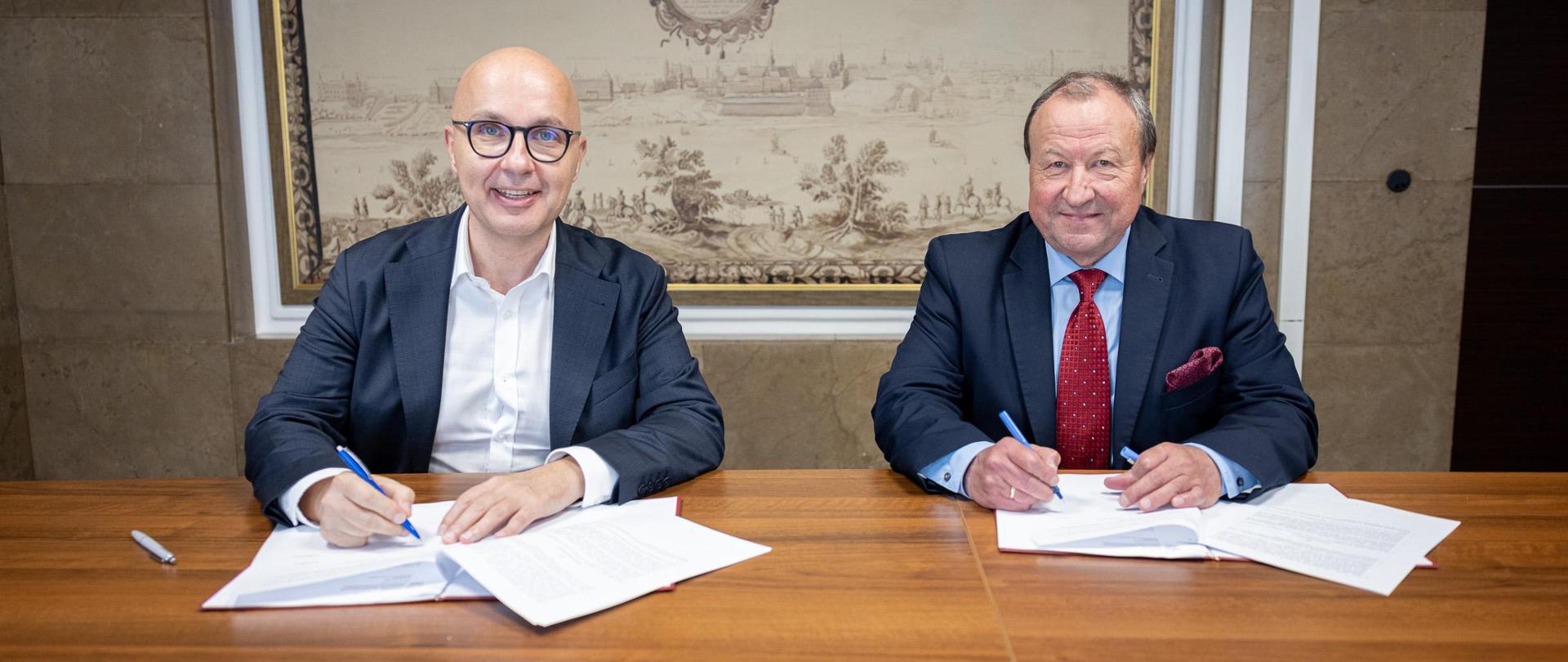 Wiceminister aktywów państwowych Robert Kropiwnicki oraz Prezes Zarządu spółki Zarządca Rozliczeń S.A. Jan Bogolubow podpisują umowę w zakresie współpracy dotyczącej realizacji zapisów ustawy z dnia 17 sierpnia 2023 roku i osłon socjalnych dla pracowników sektora elektroenergetycznego oraz branży górnictwa węgla brunatnego. Zdjęcie w trakcie podpisania. 