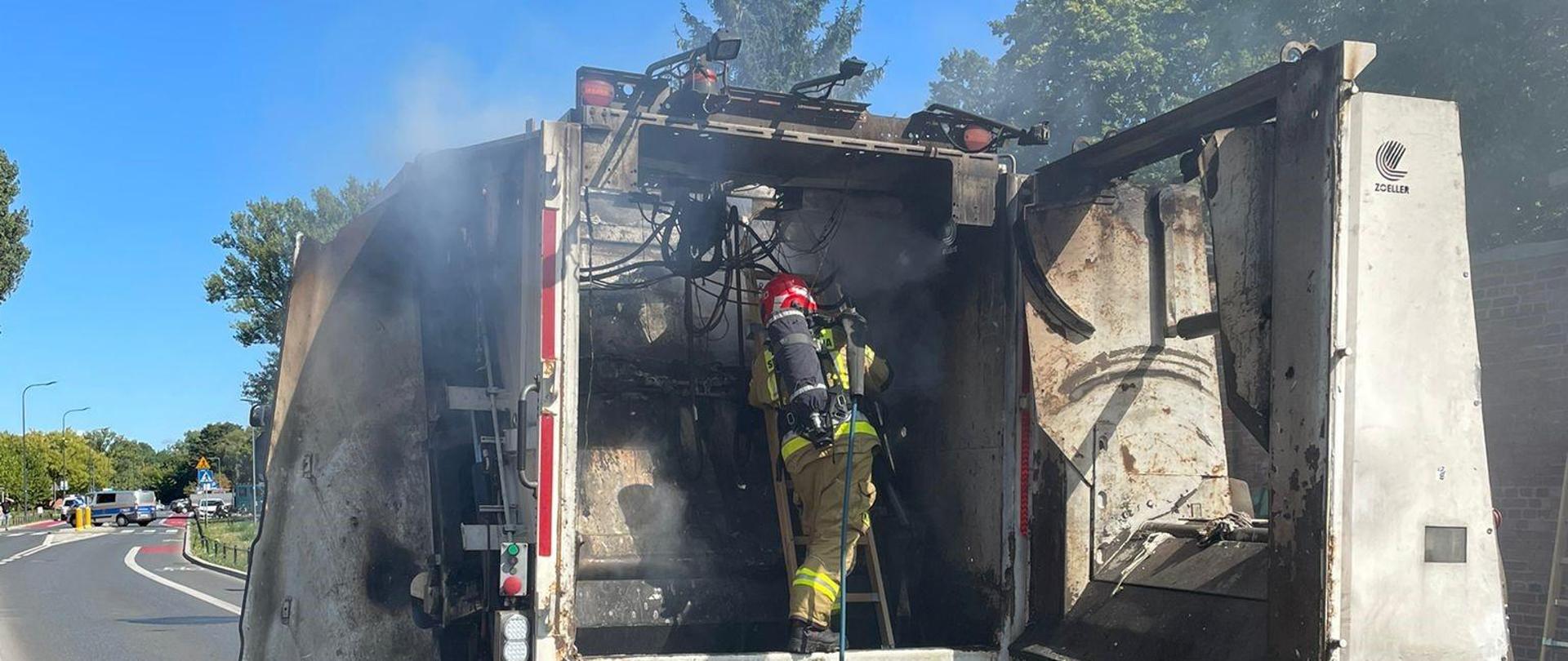 Funkcjonariusz w trakcie gaszenia pożaru w środku śmieciarki