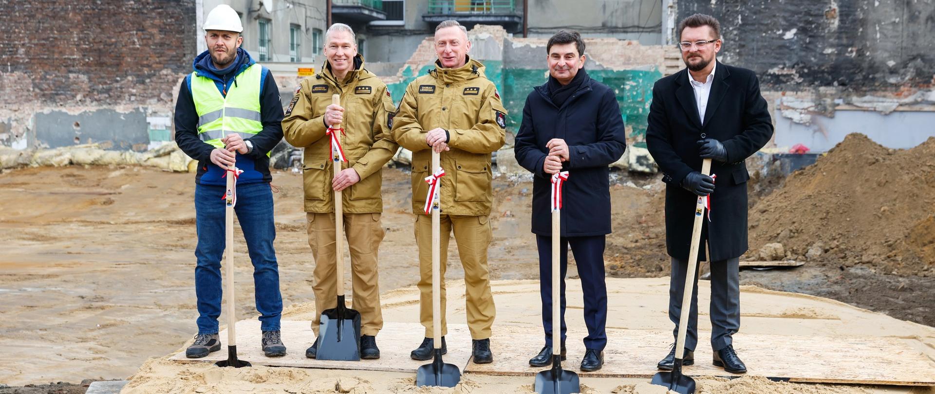 Wojewoda Śląski, Śląski Komendant Wojewódzki Prezydent Miasta Katowice oraz Komendant Miejski PSP w Katowicach, przedstawiciel firmy budowlanej na tle budowanej nowej Jednostki Ratowniczo-Gaśniczej nr 3 z symboliczną wkopaną pierwszą łopatą.