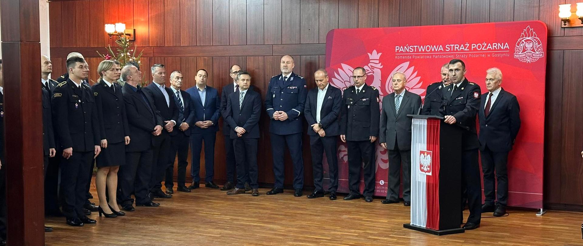 Podczas spotkania przemawia komendant. W tle stoją zaproszeni goście.