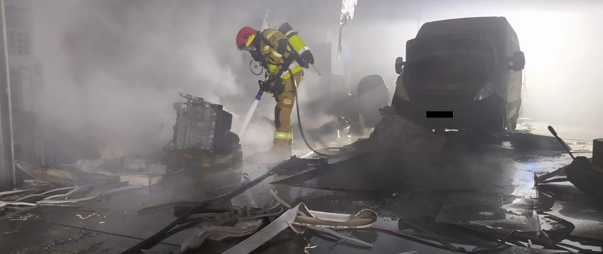 Na zdjęciu widnieje strażak w trakcie gaszenia pożaru warsztatu samochodowego. 
