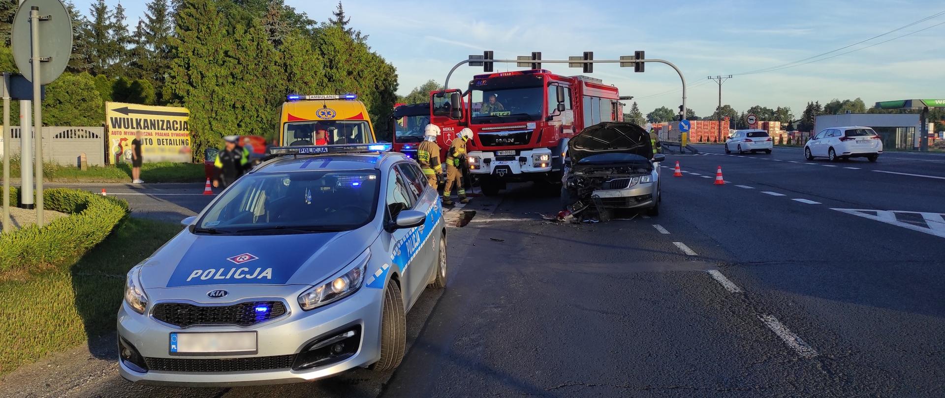Zdjęcie przedstawia radiowóz policyjny, obok rozbity samochód osobowy, wóz strażacki i karetkę pogotowia