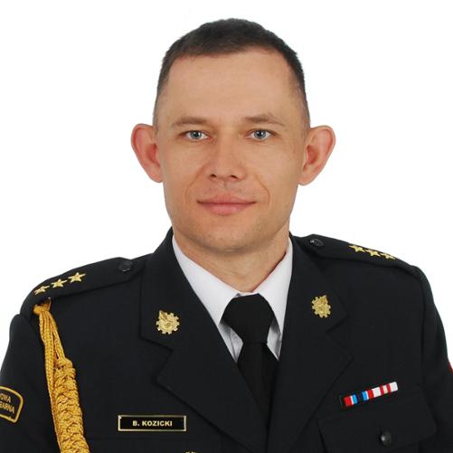 Zdjęcie przedstawia uśmiechniętego w średnim wieku mężczyznę na białym tle w mundurze galowym. 