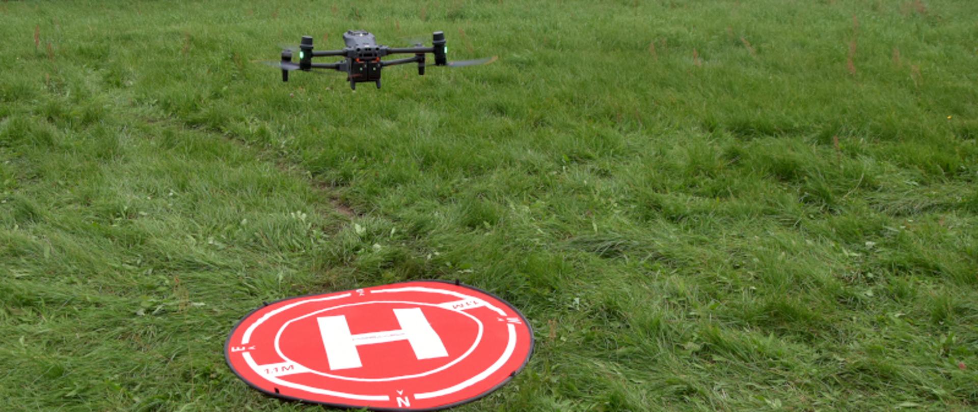 dron uniesiony ponad czerwoną, okrągłą matę położoną na zielonej trawie