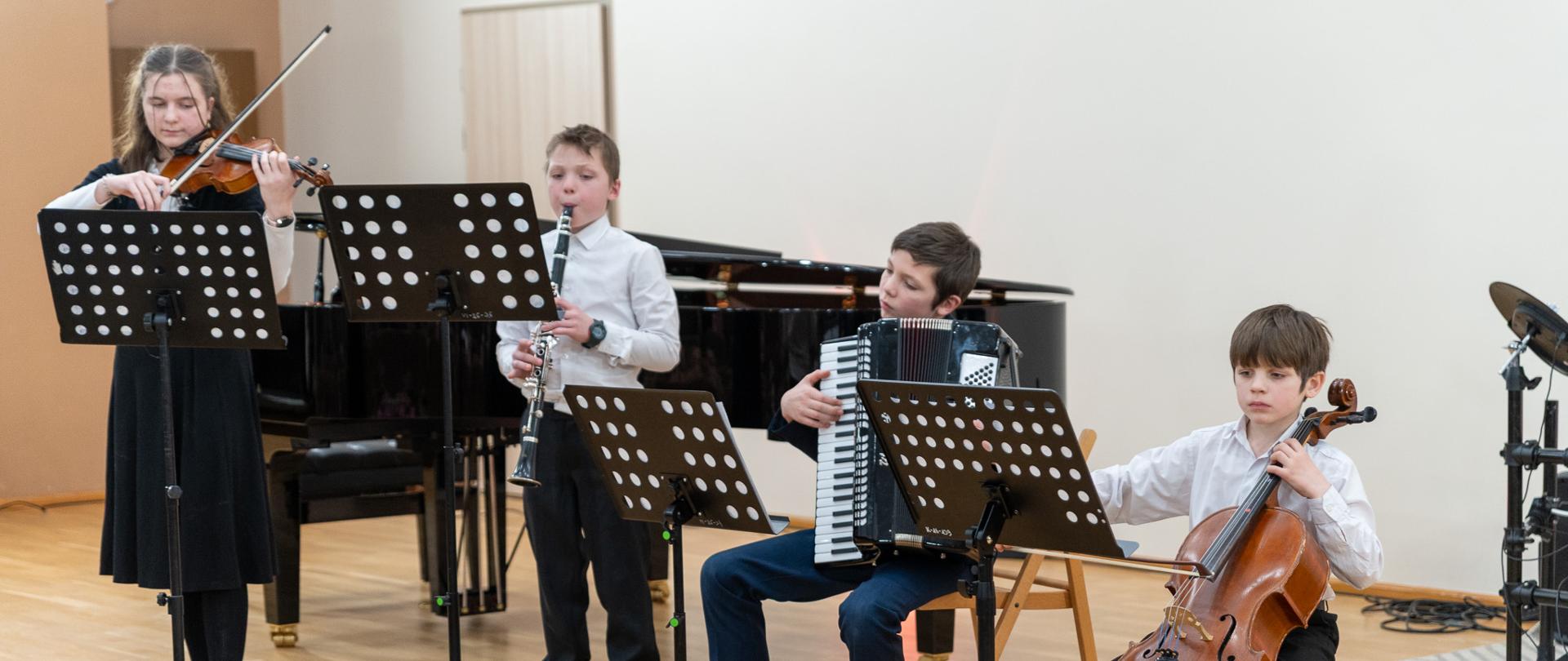 Na scenie sali koncertowej PSM czwórka rodzeństwa Szczepaniak wykonuje utwór w kwartecie (skrzypce, klarnet, akordeon, wiolonczela).